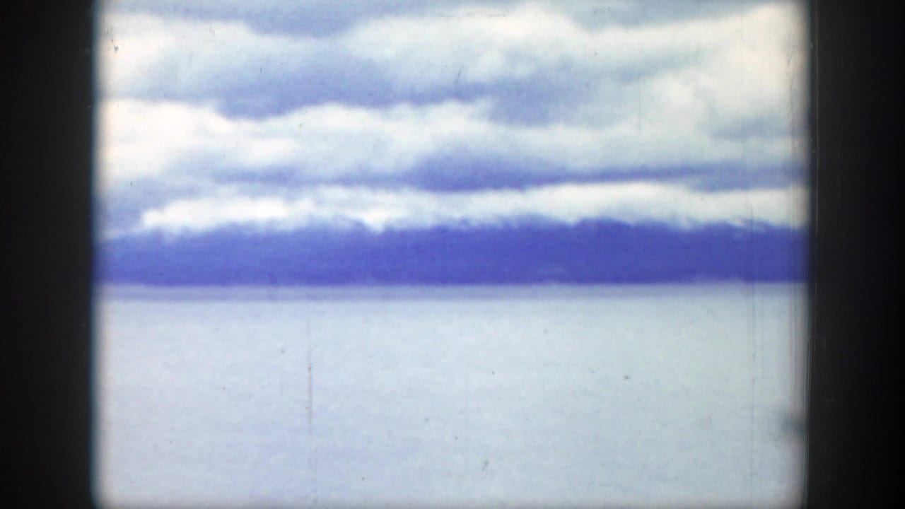 Cloudy sky over pale water with a dark mountain horizon.