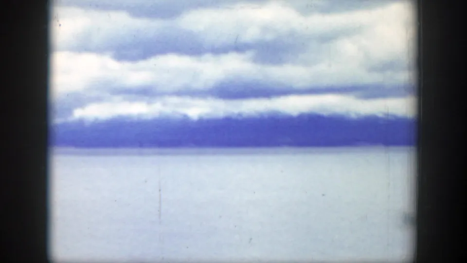 1939 Wyoming home-movie frame showing layered clouds above pale water and distant dark mountains.