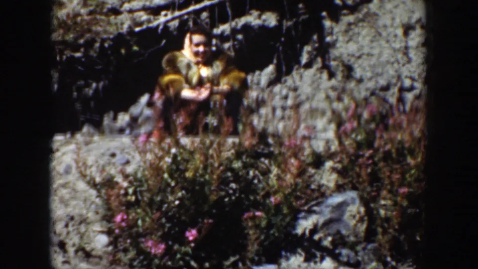 A woman in period-looking clothing sits among rocks and wildflowers in the Wyoming landscape.