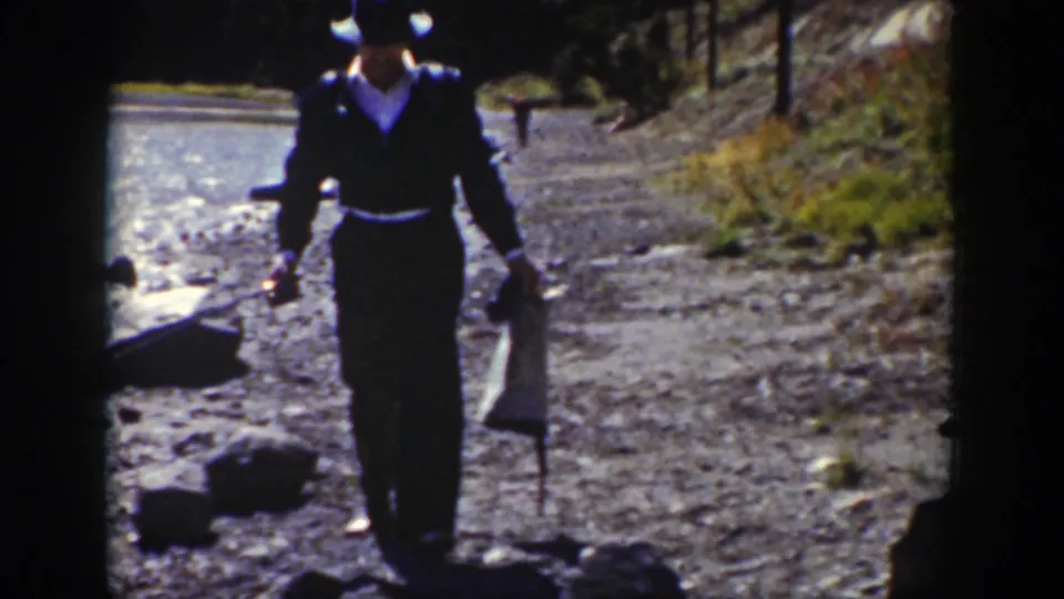 Near the end of the 1939 Wyoming clip, the man walks toward the camera with a bag and long object beside the stream.