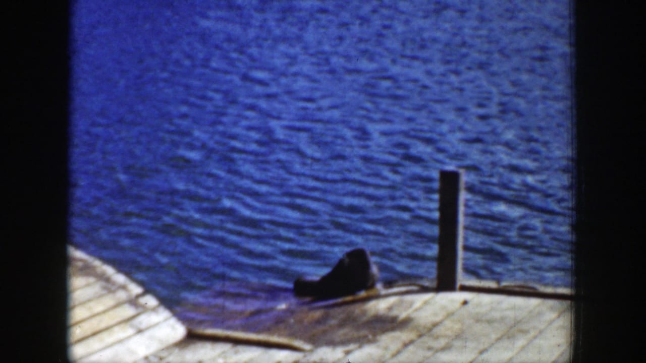 1939 Wyoming 8mm frame focused on blue water, a wood dock or ramp, a vertical post, and a dark animal resting near the edge.