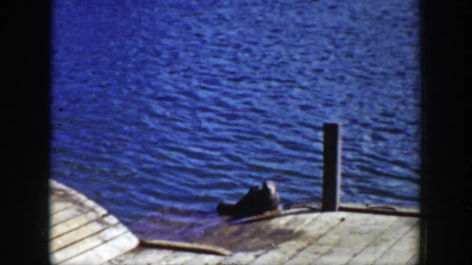 1939 Wyoming 8mm frame with rippled blue water, weathered wood boards, a post, and a seal-like dark animal near the dock edge.