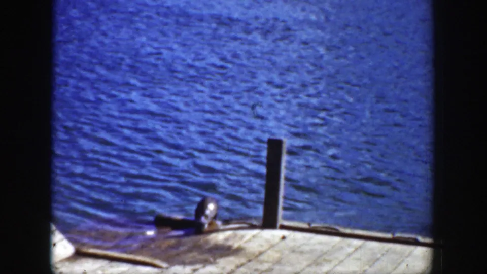 1939 Wyoming 8mm frame showing a dark seal-like animal near a dock post, with blue water and weathered boards in view.