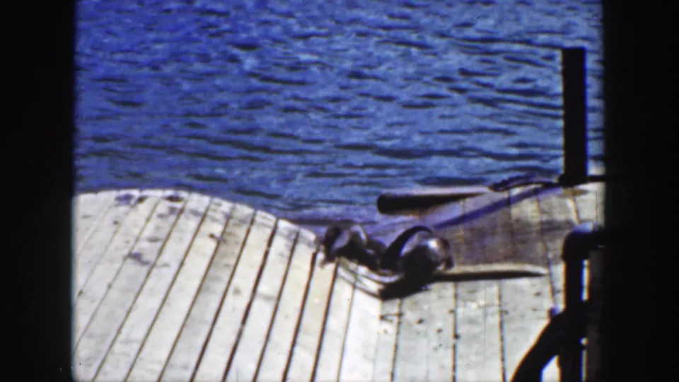 1939 Wyoming 8mm frame showing sea lions near the dock edge, with blue water, planked boards, and dark posts visible.