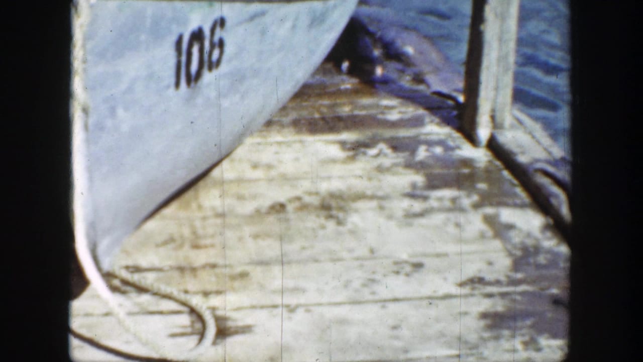 Numbered boat beside a weathered wooden dock in bright sunlight.