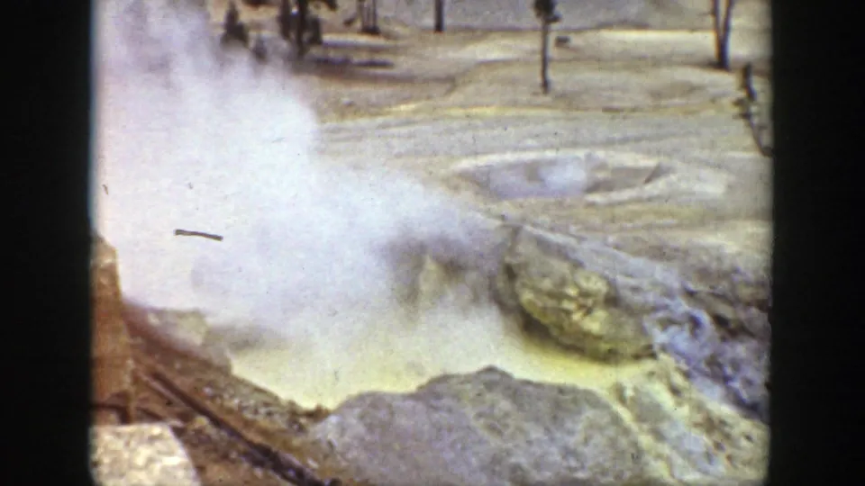 1939 Wyoming frame with steam lifting from a sulfur-colored geothermal pool beside mineral deposits and sparse trees.