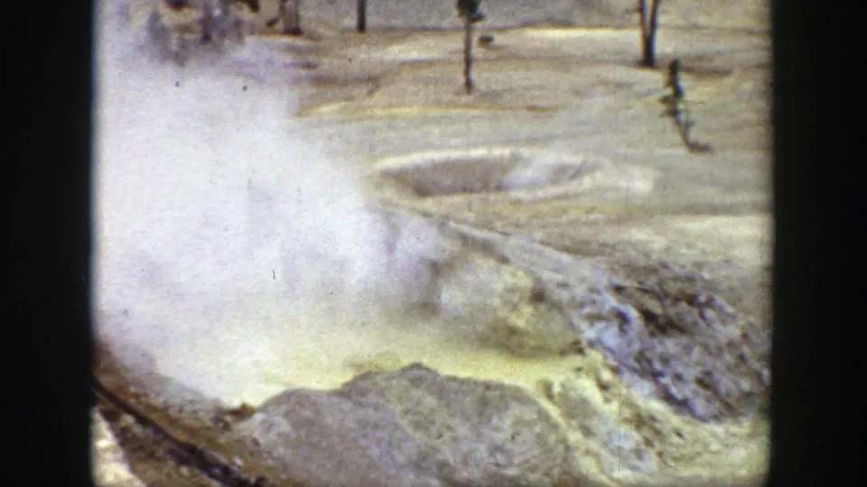 1939 Wyoming frame showing drifting steam over a yellow geothermal pool, rocky margins, and sparse trees beyond the basin.