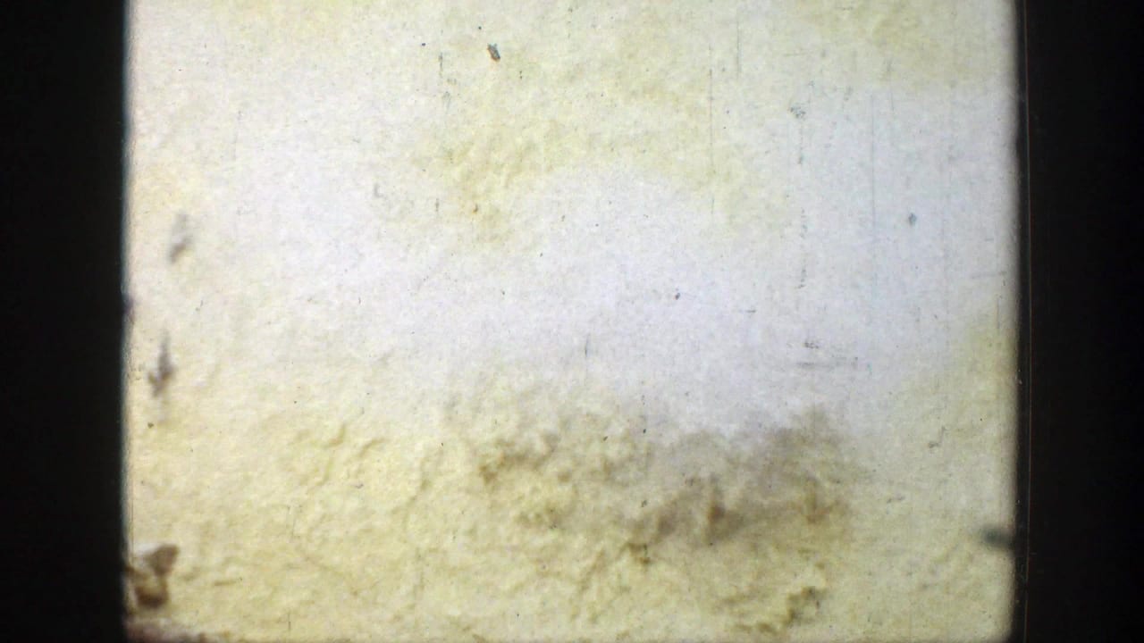 Pale scratched film frame with dark gate edges and little visible scene detail.