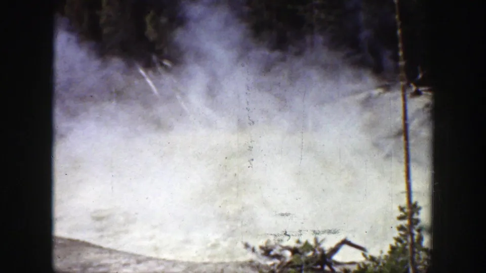 Dense vapor rises in a Wyoming geothermal setting, with evergreen trees partly visible through soft, faded 8mm color.