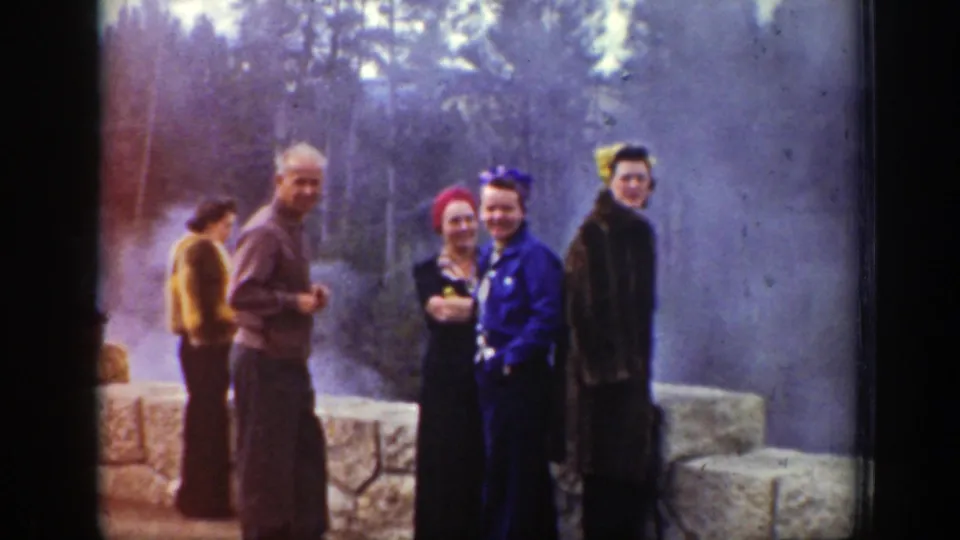 Group of adult tourists at a Wyoming geyser overlook, including women in bright head coverings and coats, with steam and trees behind them.