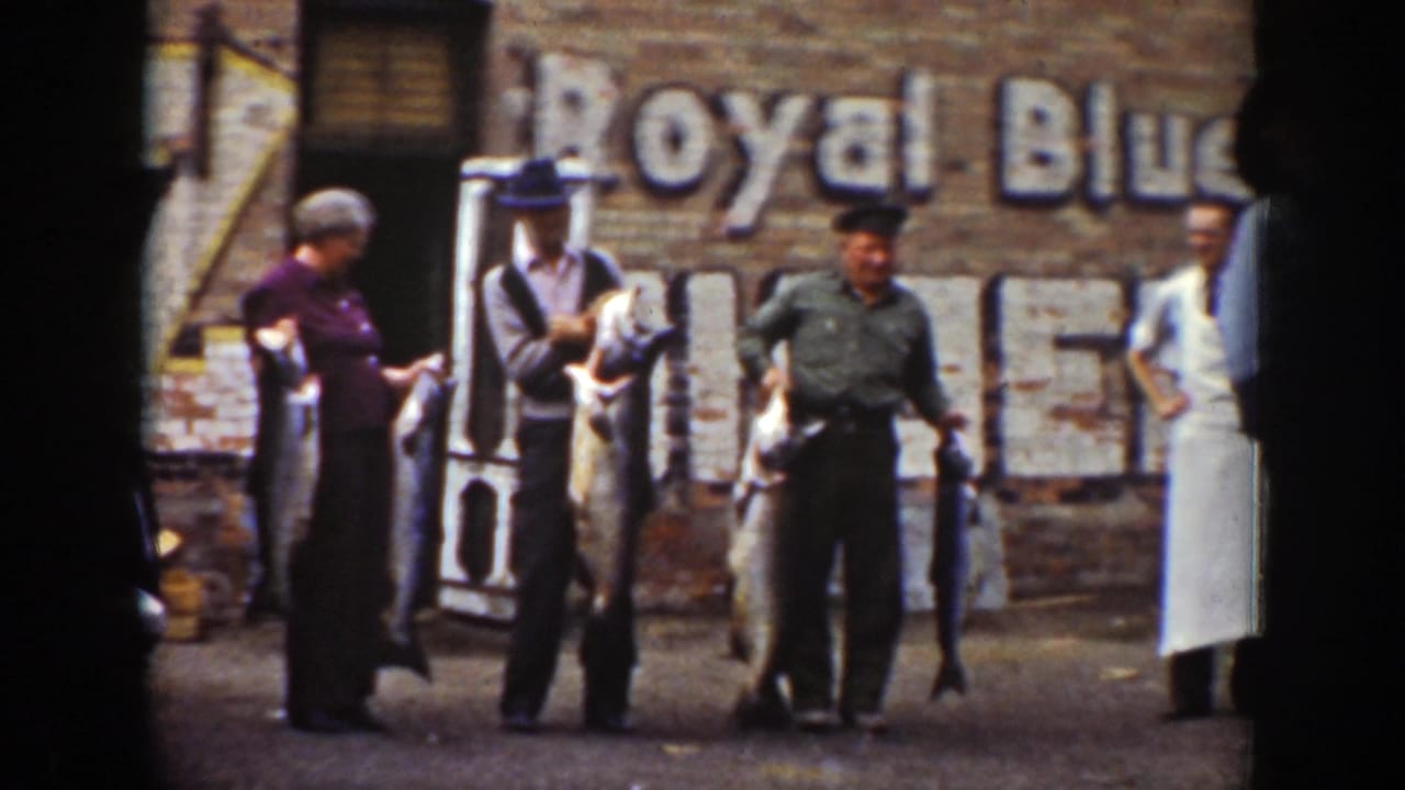 Three adults hold large fish in front of a brick wall with a faded sign.