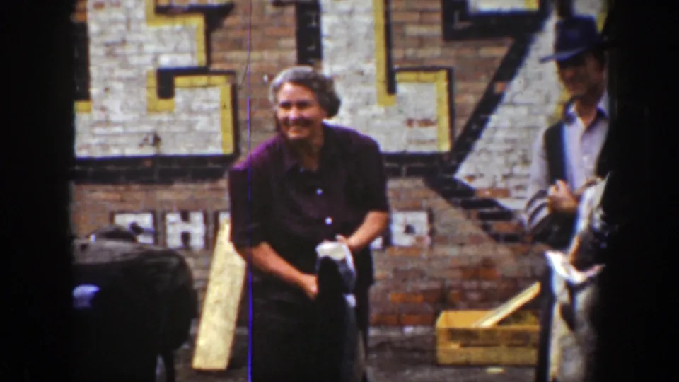 In 1939 Wyoming home-movie footage, adults gather by a brick wall as a smiling woman in a dark blouse holds a fish.