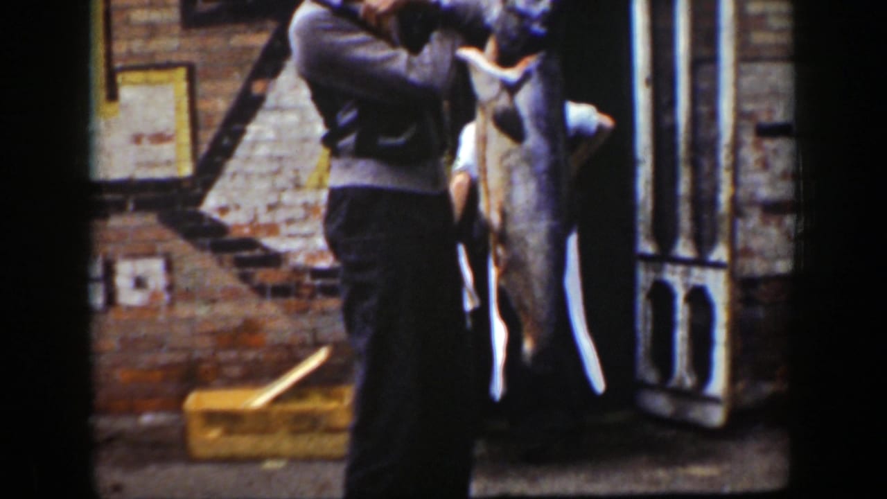 Woman holding a large fish near a house exterior as another person stands close by.