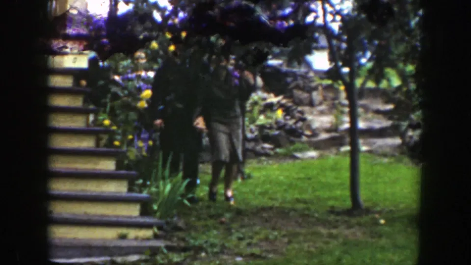 The couple moves near a short set of garden steps, partly hidden by foliage and dark frame edges in the 8mm scan.