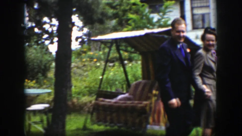 The couple passes a striped garden swing in the 1939 Wyoming scene, with trees, flowers, and lawn visible around them.