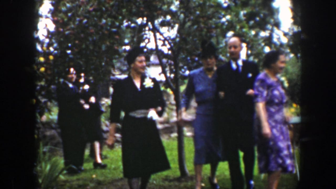 In 1939 Wyoming home-movie footage, adults in suits, dresses, and hats arrive through a garden or orchard.