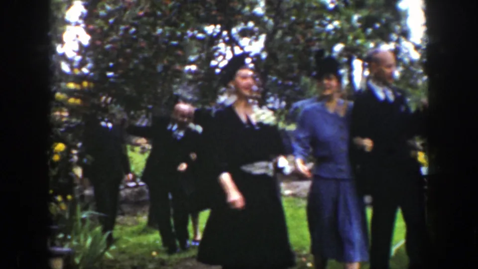 Guests in formal 1930s-style clothing move through a Wyoming garden, with one woman in front and others behind her.