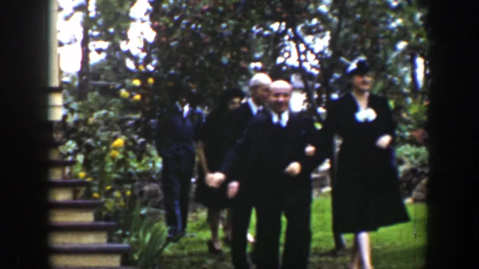 In 1939 Wyoming home-movie footage, formally dressed adults gather in a leafy garden, with men in suits and women in dark dresses.