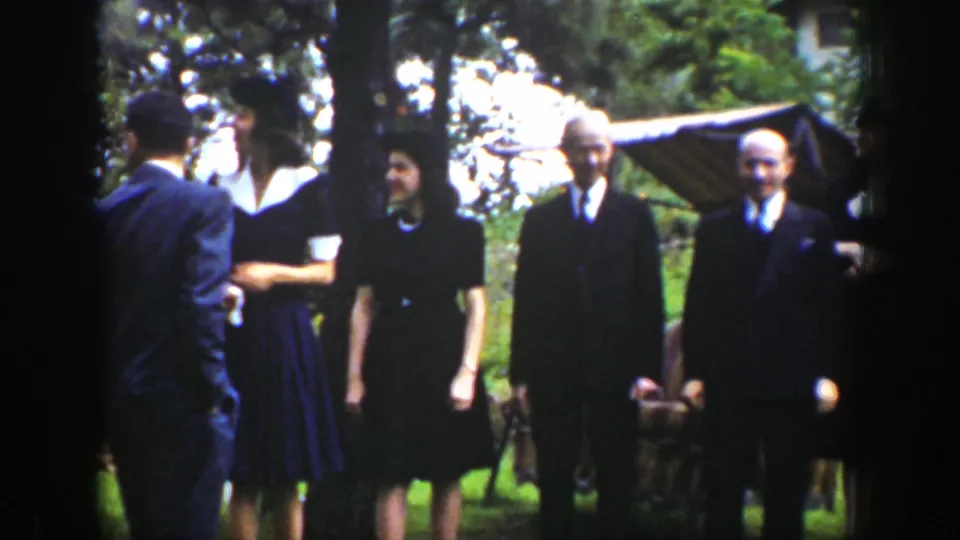 A man seen from behind approaches formally dressed guests standing on a garden lawn in 1939 Wyoming footage.
