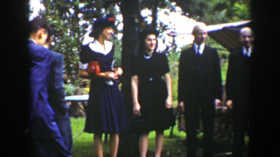 Formally dressed adults stand together in a leafy garden, including women in hats and men in suits, in 1939 Wyoming footage.
