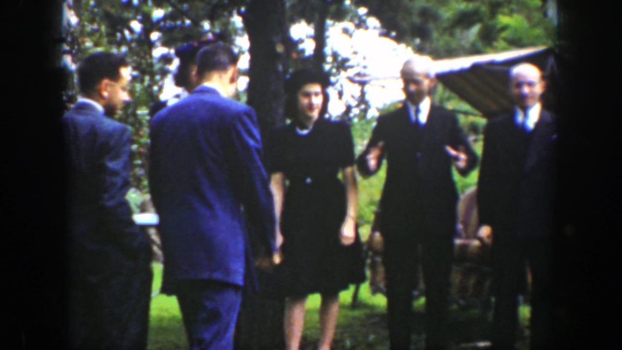 Formally dressed adults stand outdoors on a shaded lawn.