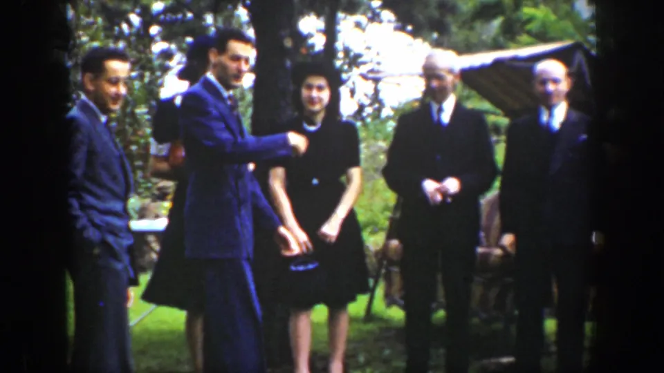 A suited man gestures toward the camera as adults in formal clothing stand outdoors in 1939 Wyoming footage.