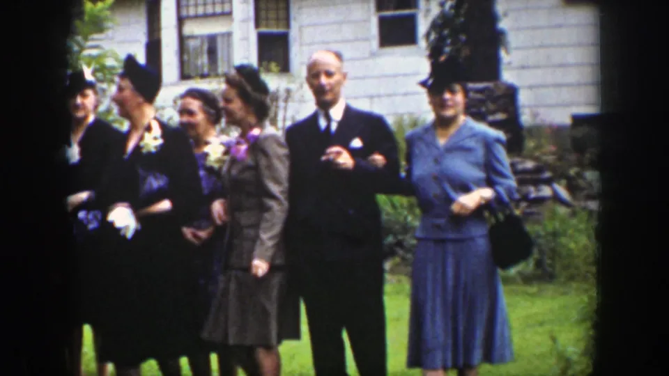 Formally dressed adults, including women in hats and a man in a suit, stand outside near a building in Wyoming.