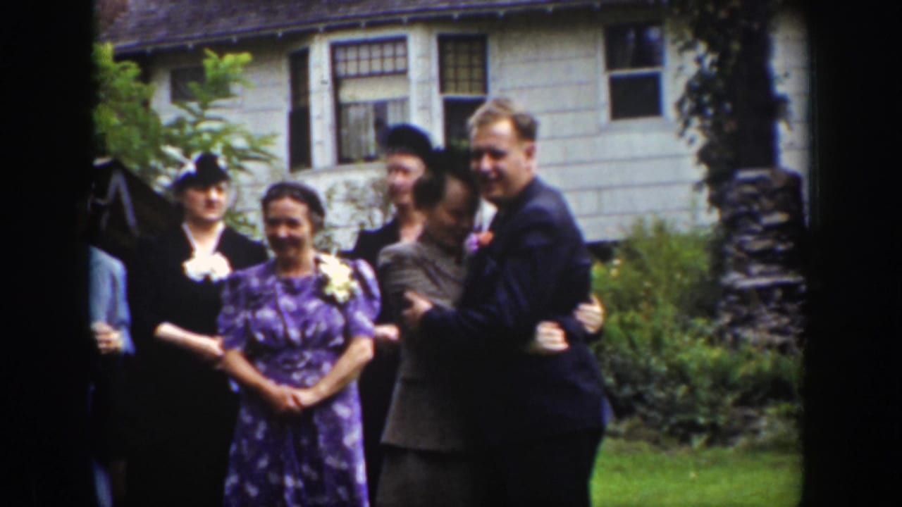 Group of adults in formal clothing gather on a lawn in front of a house.