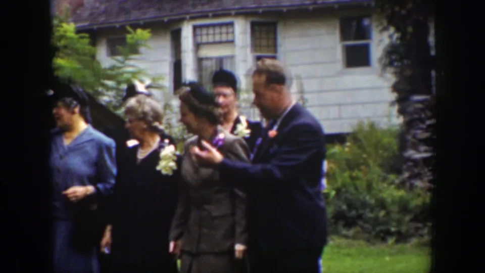 1939 Wyoming home-movie frame of adults in period dress moving across a lawn after a social greeting outside a house.