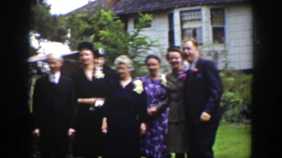 Formally dressed adults smile and pose on a Wyoming lawn in 1939, with flowers, hats, and a house exterior visible behind them.