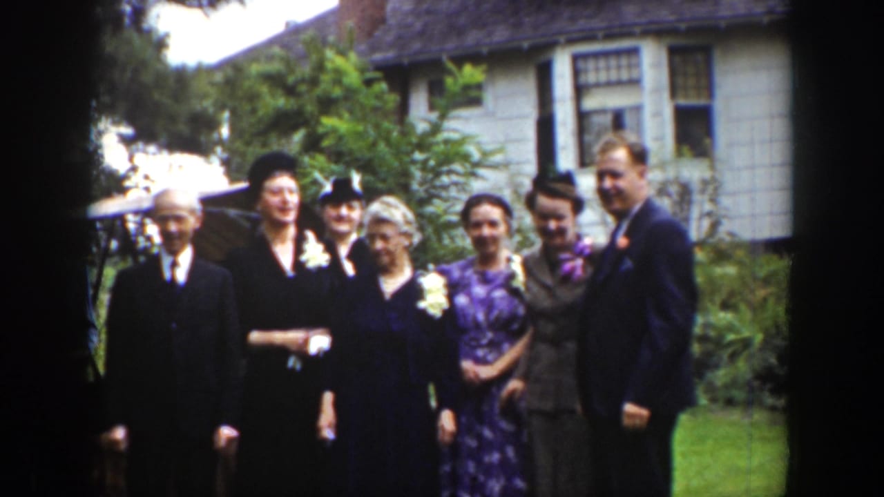 Adults in formal clothing pose on a lawn in front of a house.