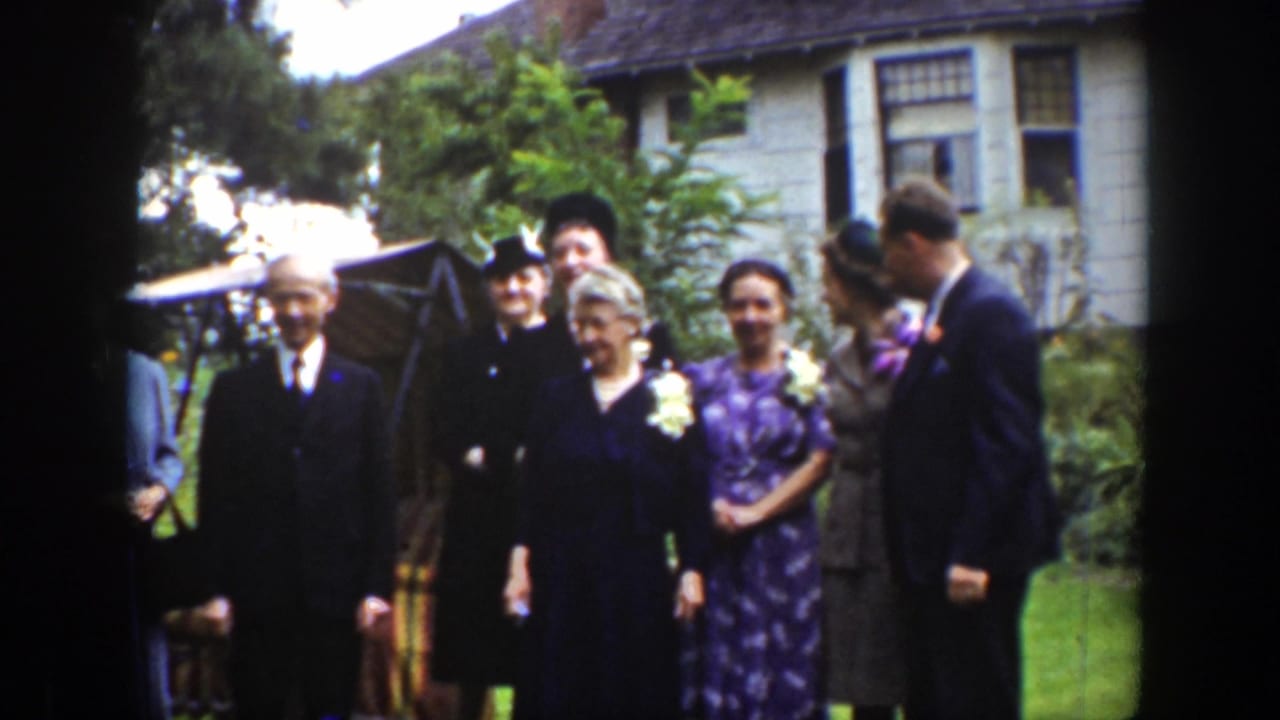 Formal adult group stands on a lawn near shrubs and a house.
