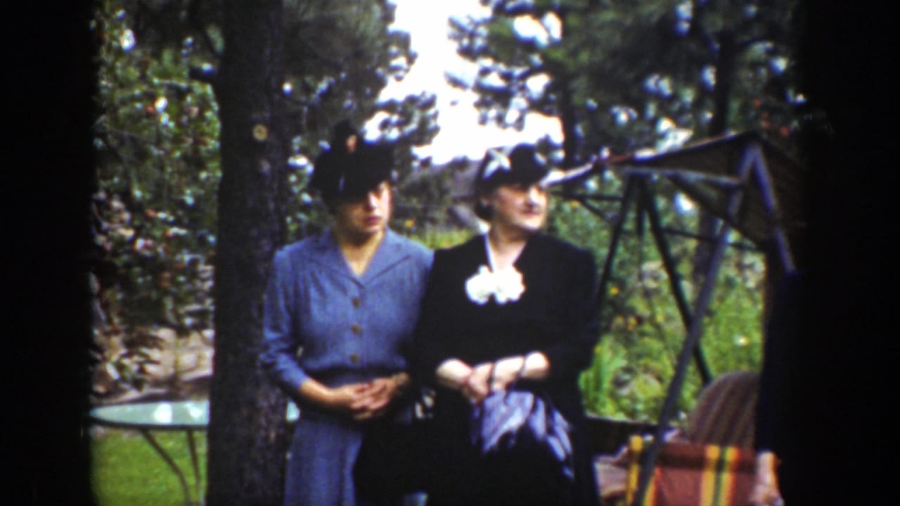 Two women in hats stand beside a tree with a swing and chair in the background.