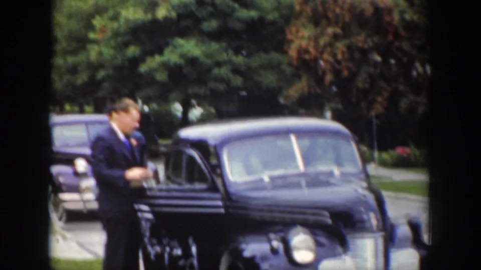 In Wyoming, 1939, a suited man stands near a dark blue wedding sedan marked for a newly married couple.
