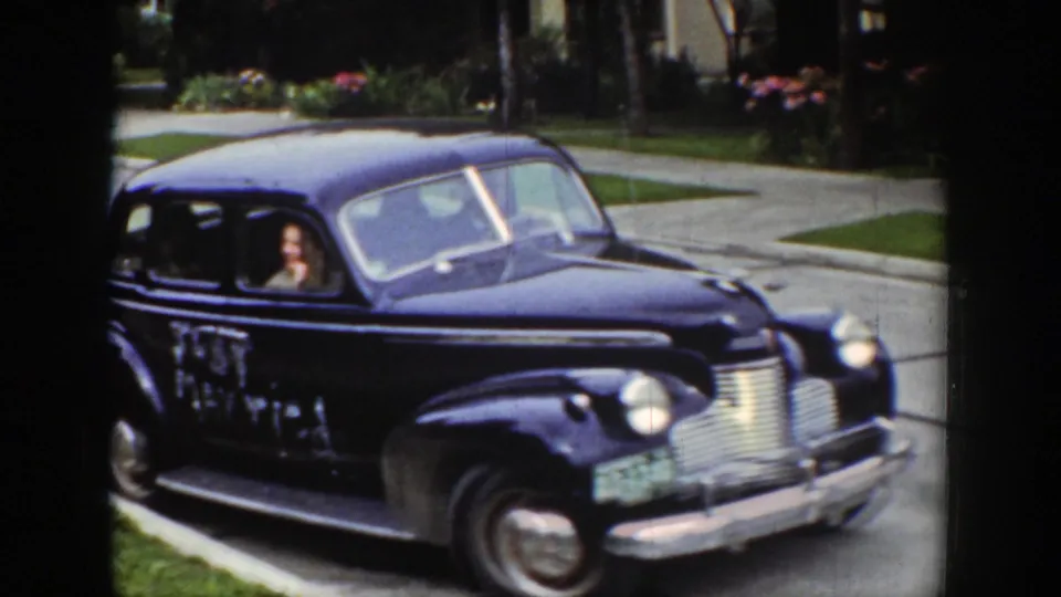 The 'Just Married' sedan passes along the Wyoming street, showing white writing on the side and a passenger at the window.