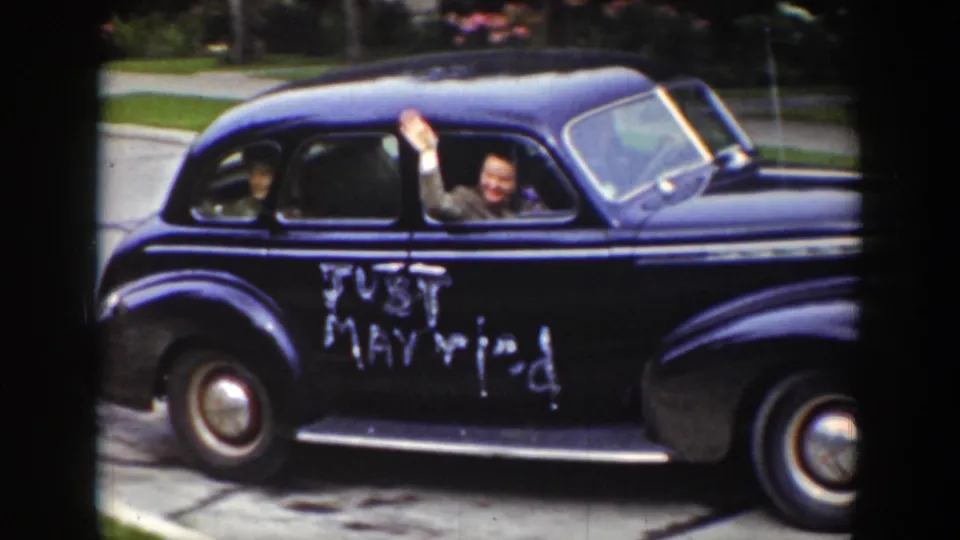 A passenger waves from the rear window of the dark blue Just Married car as it drives past in Wyoming, 1939.