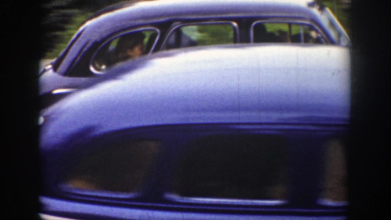 A soft 8mm frame shows the side of the wedding sedan with occupants faintly visible, partly blocked by a light-colored car crossing the foreground.