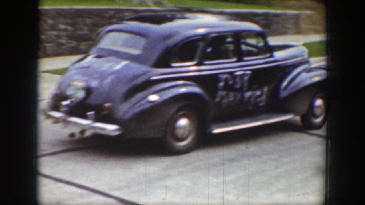 Rear-side view of the decorated sedan moving along a residential road.
