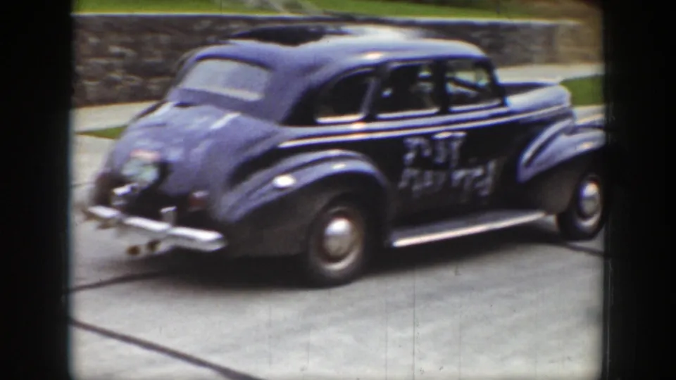 The decorated 1939 wedding car is seen from the rear side on a paved neighborhood road, with the Just Married message still visible on the door area.