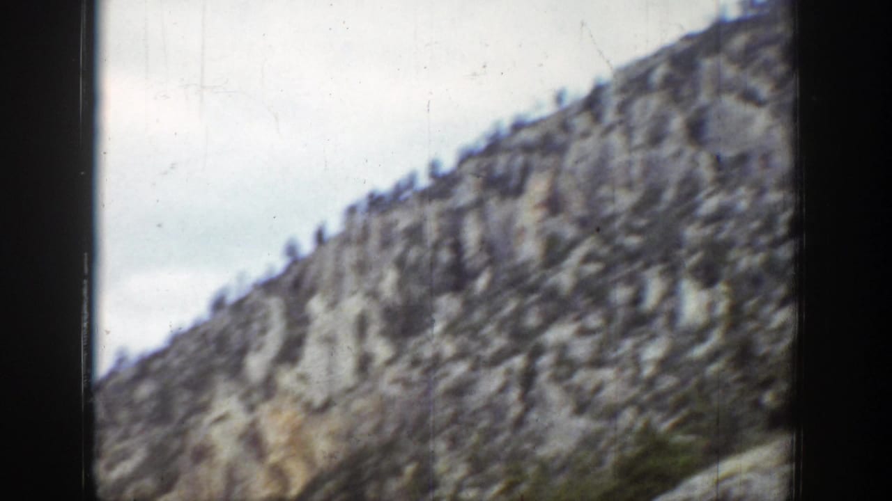 1939 Wyoming 8mm view of a steep gray rock slope with evergreens scattered near the ridge line.