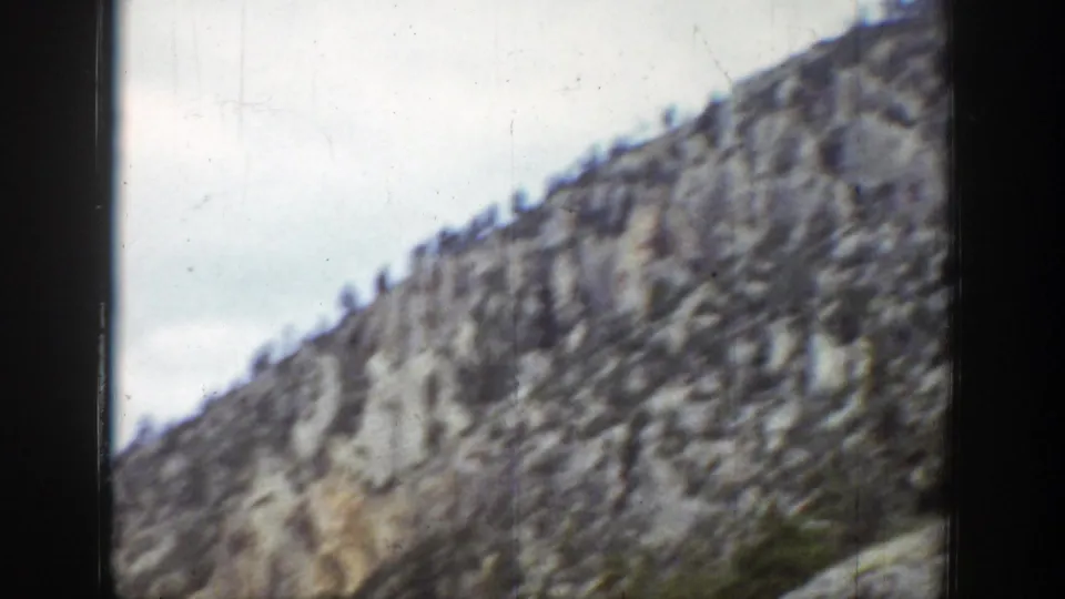 1939 Wyoming 8mm view of a steep gray rock slope with evergreens scattered near the ridge line.