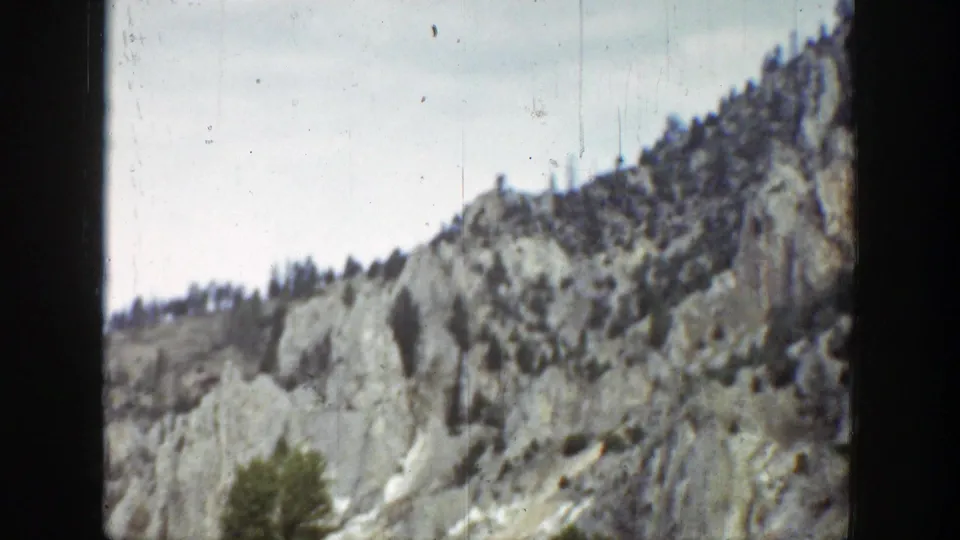 1939 Wyoming 8mm frame showing rugged hillside rock, sparse evergreen growth, and a muted overcast sky.