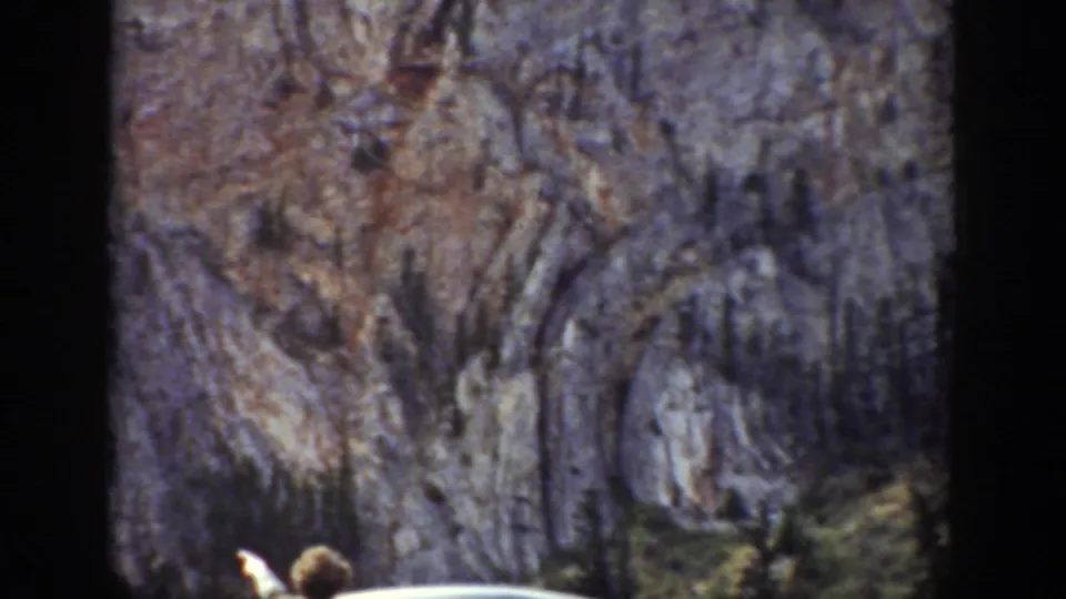 A partially visible person near the car appears to point or look upward toward steep Wyoming cliffs.