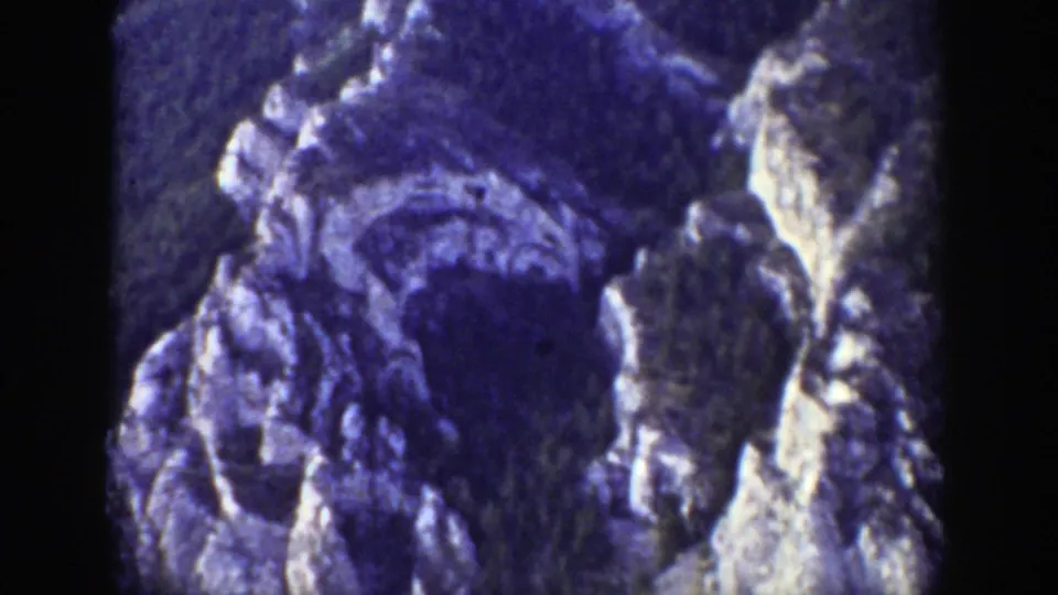 1939 Wyoming 8mm frame with craggy pale rock formations and darker forested mountain terrain, tinted blue-purple by the film scan.