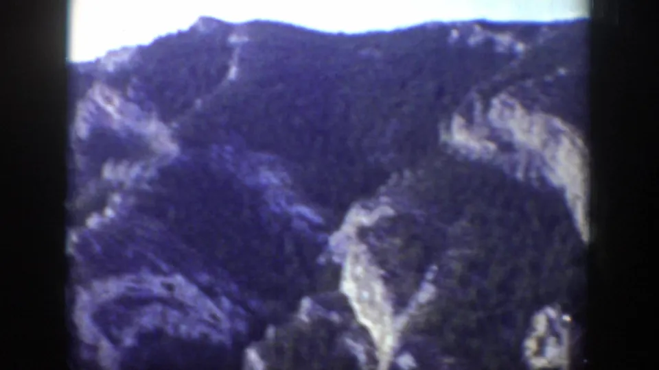 1939 Wyoming 8mm frame showing a broad mountain slope with evergreen cover, exposed rock bands, and pale sky above.