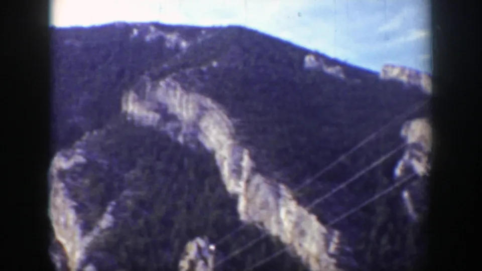 1939 Wyoming 8mm frame of a forested mountain ridge with pale exposed rock, bright sky, and diagonal foreground lines near the right edge.