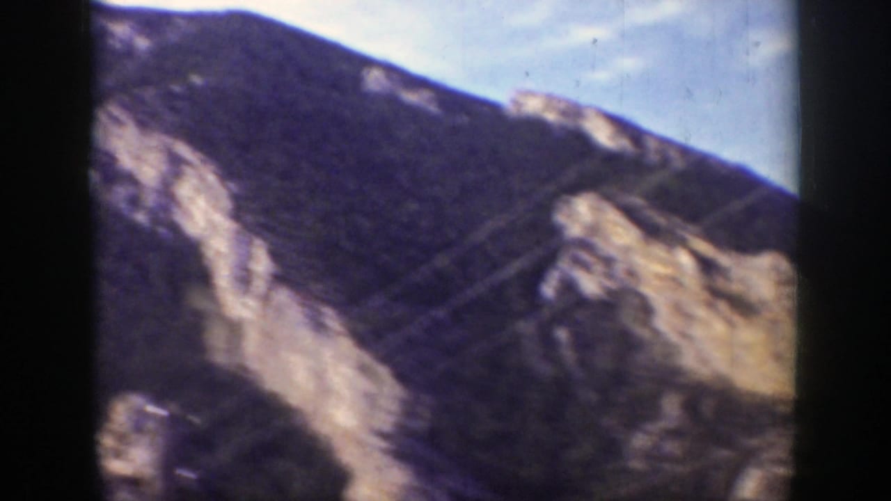 Rocky mountain slope with forested ridges and utility wires crossing the view.