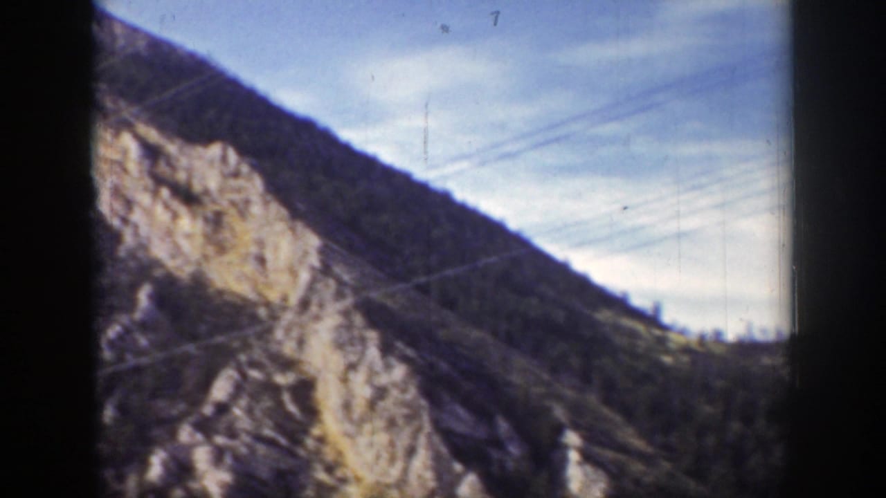 Steep cliff face and wooded ridge with power lines running diagonally across the sky.
