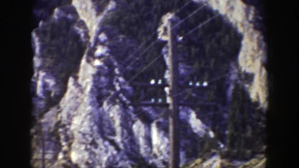 1939 Wyoming 8mm frame showing rocky cliffs, utility poles, wires, and a rail corridor through the lower valley.