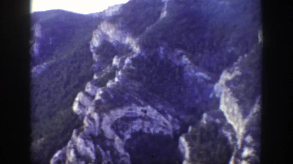 1939 Wyoming 8mm frame of a mountain valley with rocky outcrops and partial utility lines along the route.